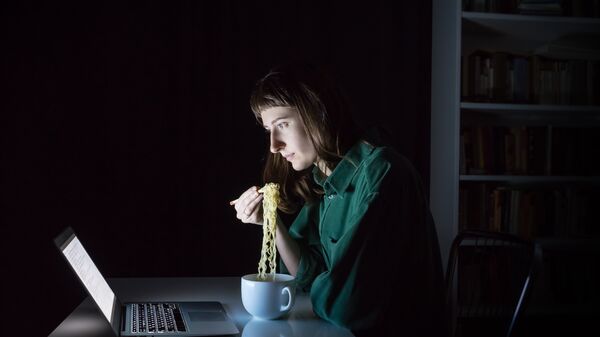 Девушка ест лапшу быстрого приготовления в темноте