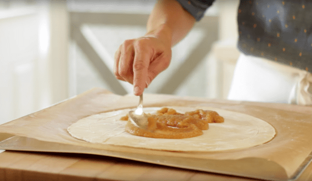 applesauce being smoothed on top of puff pastry on top of parchment paper 