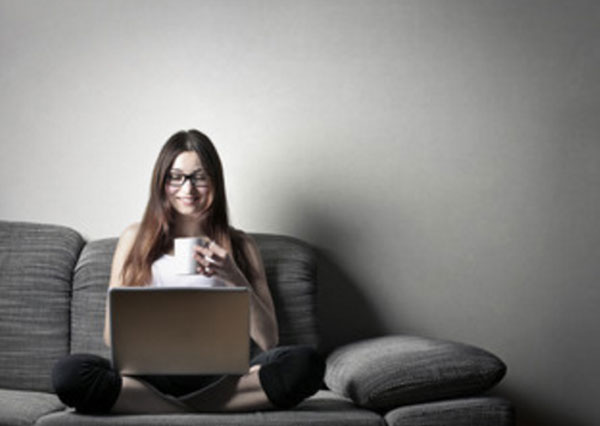 Девушка сидит на диване с ноутбуком и чашкой чая
