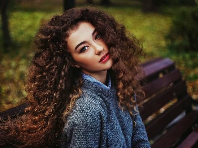 Девушка с длинными вьющимися волосами в парке на скамейке